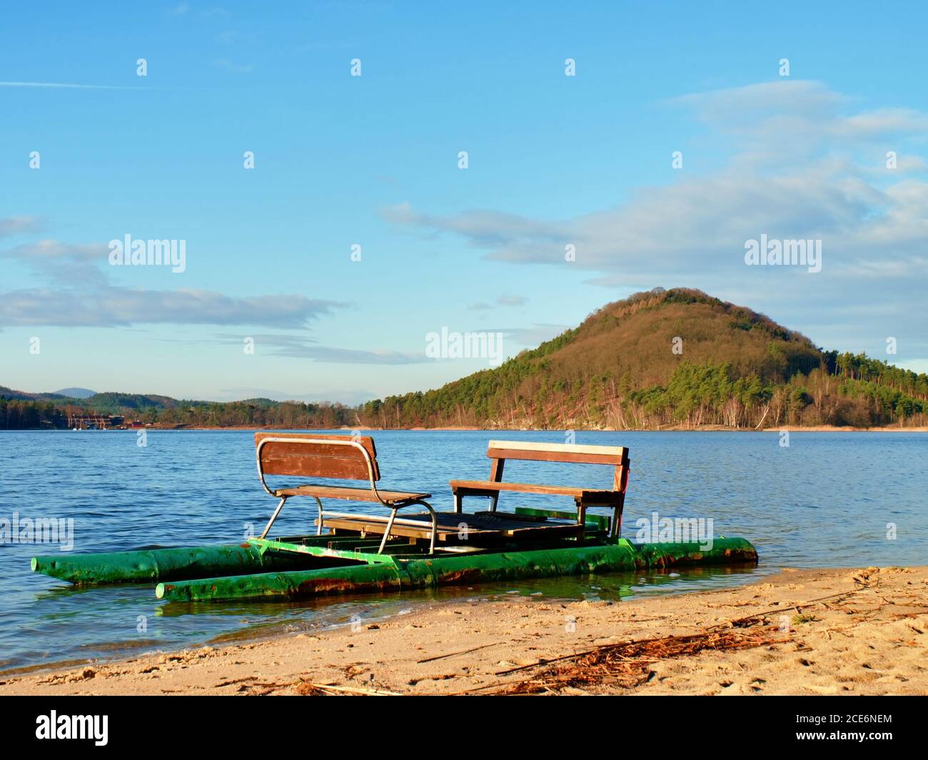Abandoned old pedal boat caught on sea sandy beach at sunset. Island with forest at horizon. Stock Photo