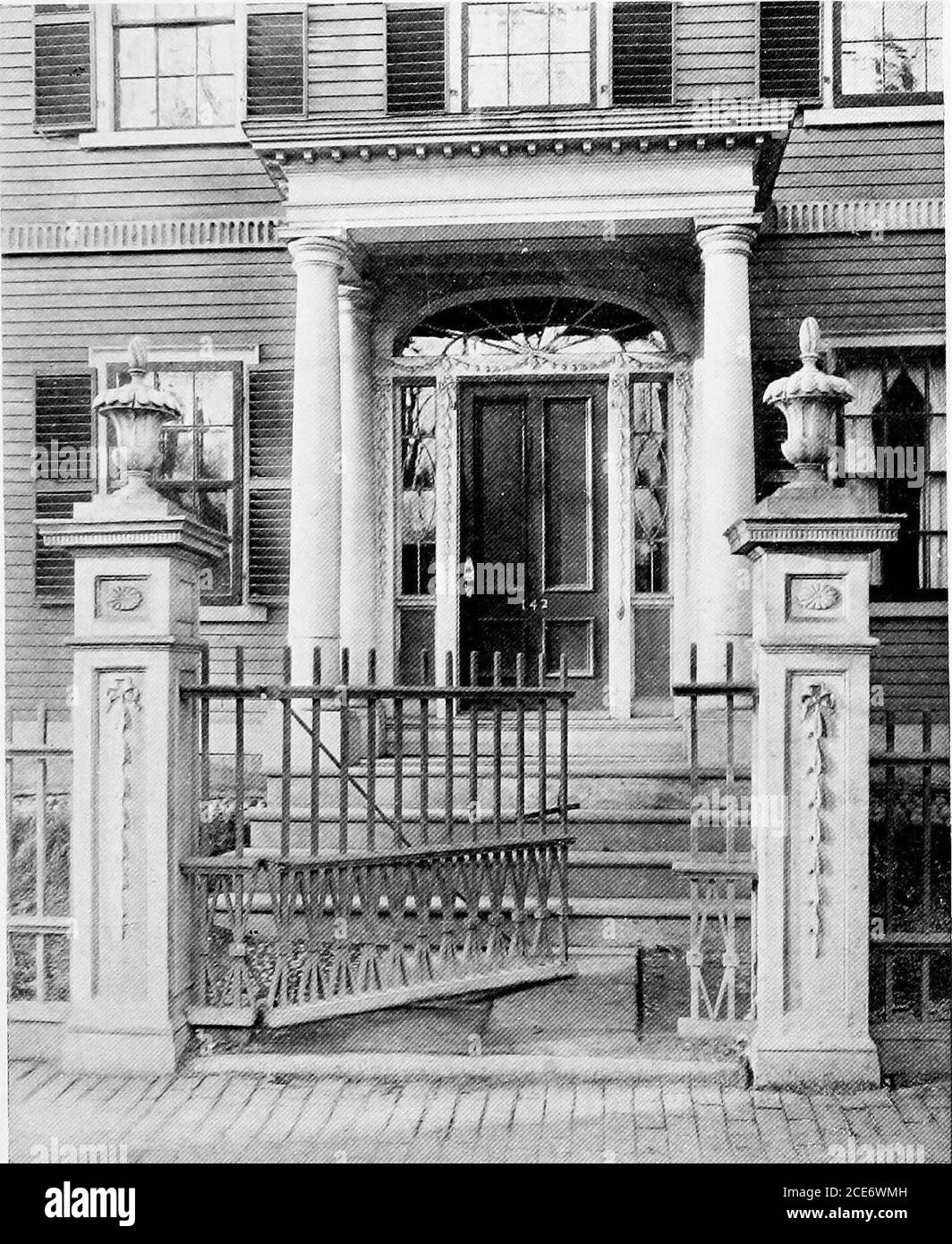 . Historic homes of New England . nence at the close of the Revolu-tionary War, a large, square house, three storiesin height, showing in exterior finish many ofMclntires best designs. The gate-posts on eitherside of the little picket gate were especially carvedfor the old Derby Mansion, as were the classiccolumns that support the porch. Not only outsidethe house but inside as well, one comes acrossMclntires wonderful carving. Step over thethreshold, enter the spacious hallway, that likemost constructed in that day extends entirelythrough the house and opens on to an old-fashionedgarden beyond Stock Photo