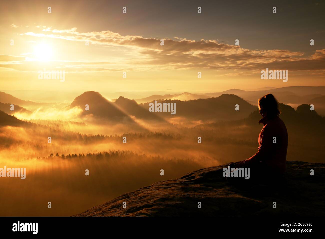 Beautiful  young long hair girl tourist enjoy daybreak on the sharp corner of sandstone rock and watch over valley to Sun. Stock Photo