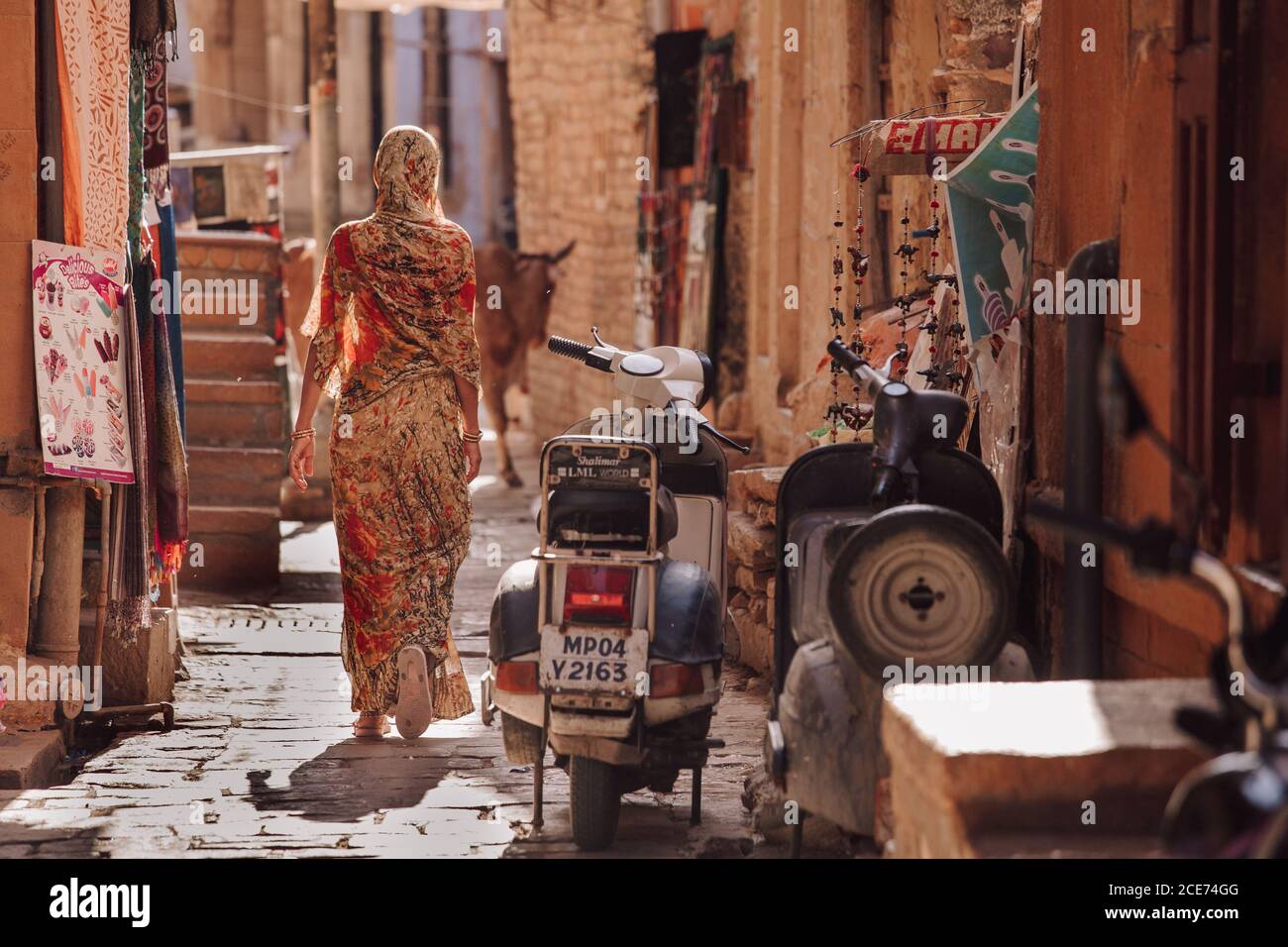 India - OCTOBER 29, 2012: Back view of unrecognizable female in traditional clothes walking near motorcycle on narrow street of old town Stock Photo