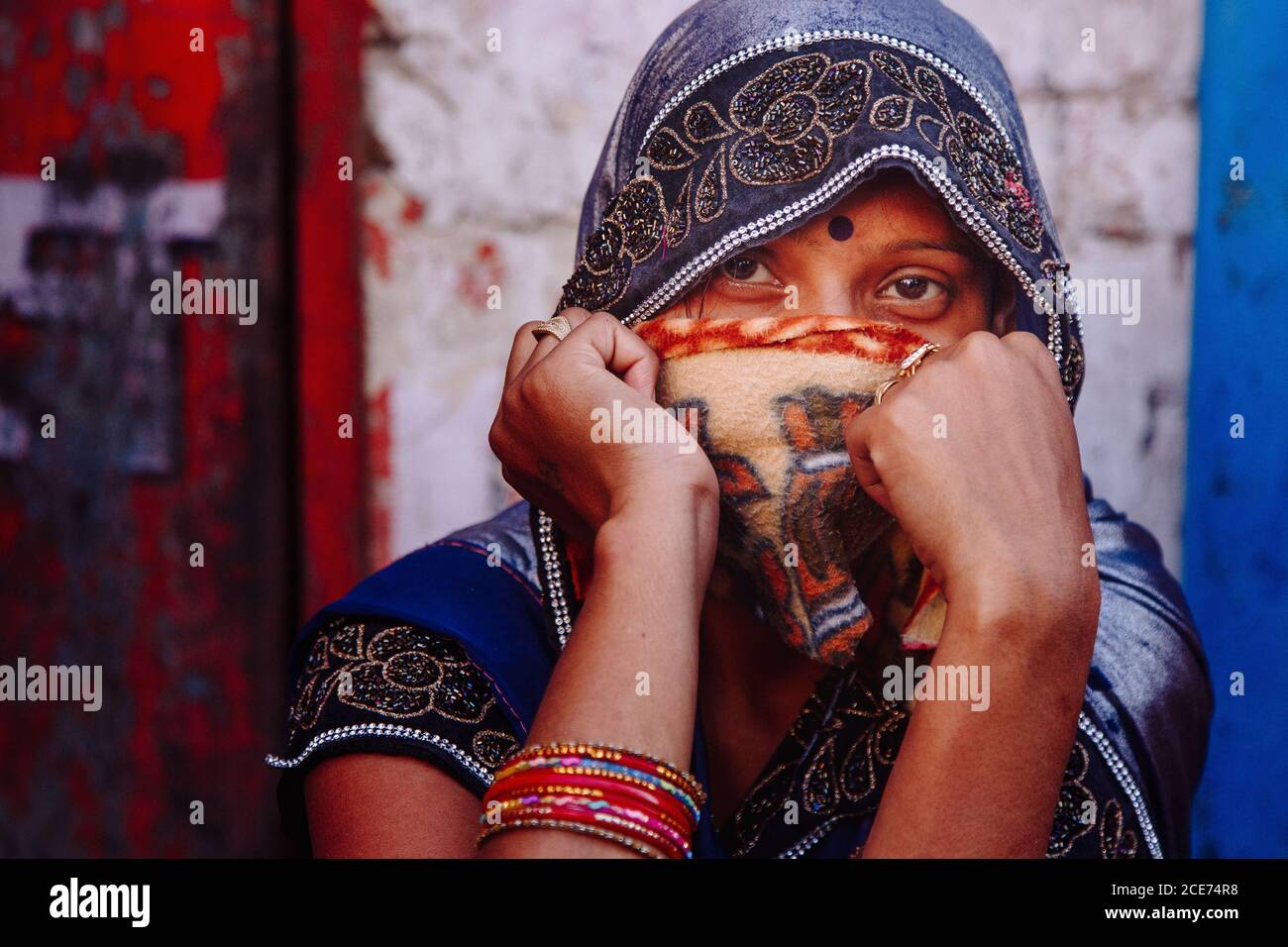 India - March 9, 2020: Charming Indian female in traditional outfit covering face and looking at camera on background of old weathered building Stock Photo
