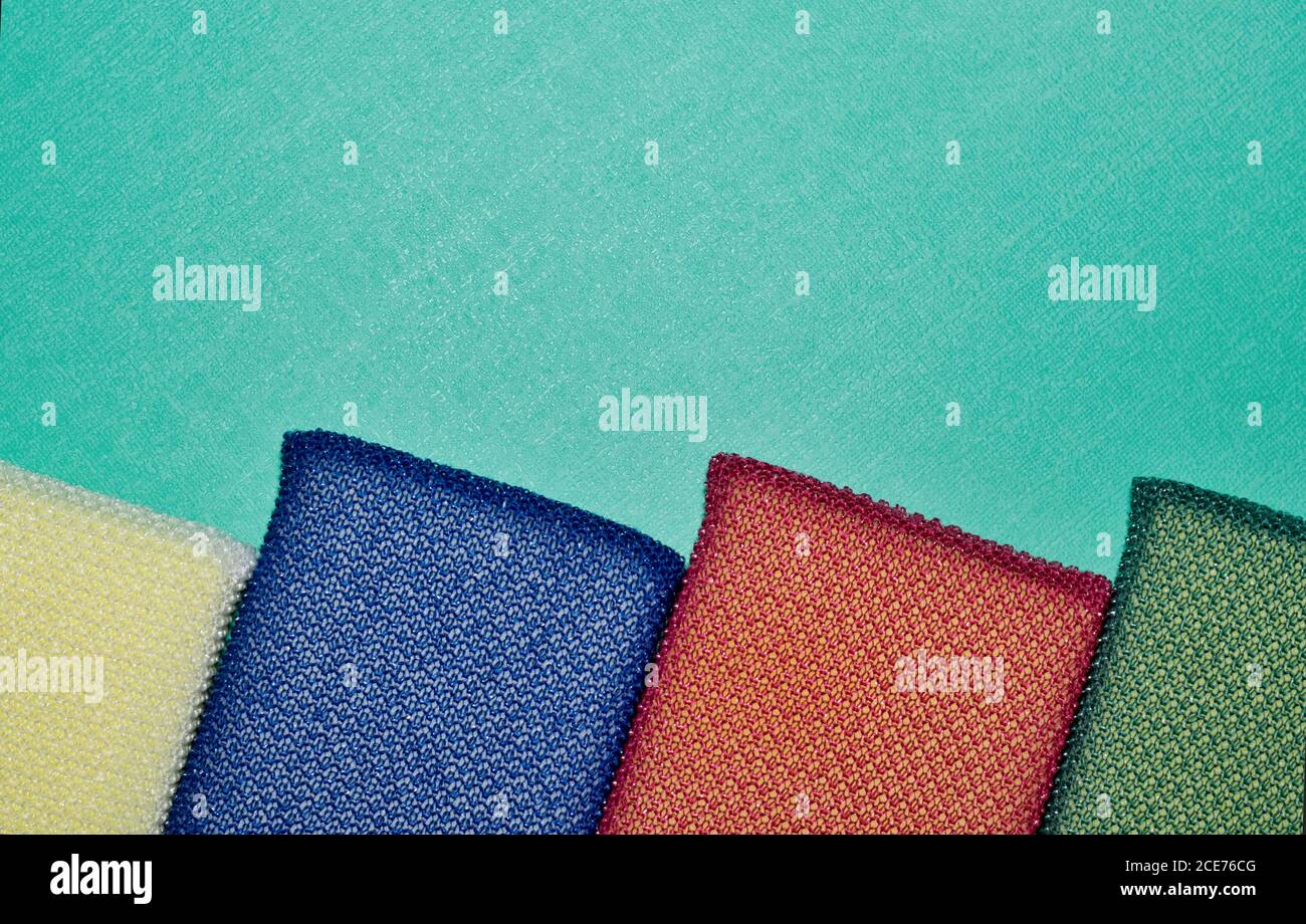 Colorful cleaning sponges lined up on a textured turquoise background with copy space above. Stock Photo
