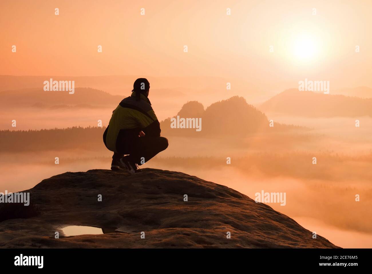 Rear view of male hiker sitting on the rocky peak  while enjoying a colorful daybreak above mounrains valley Stock Photo