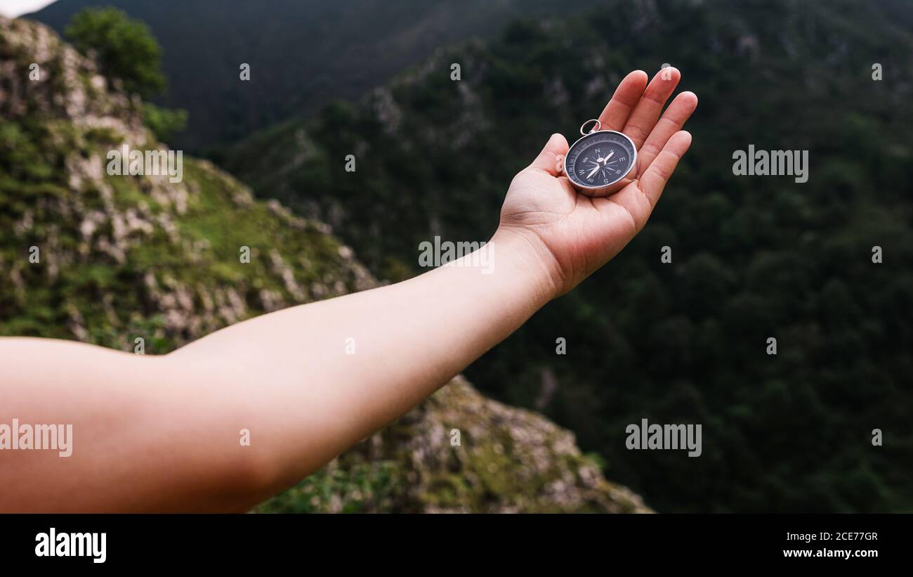 Top view of anonymous tourist standing with compass on hand on background of mountain valley Stock Photo