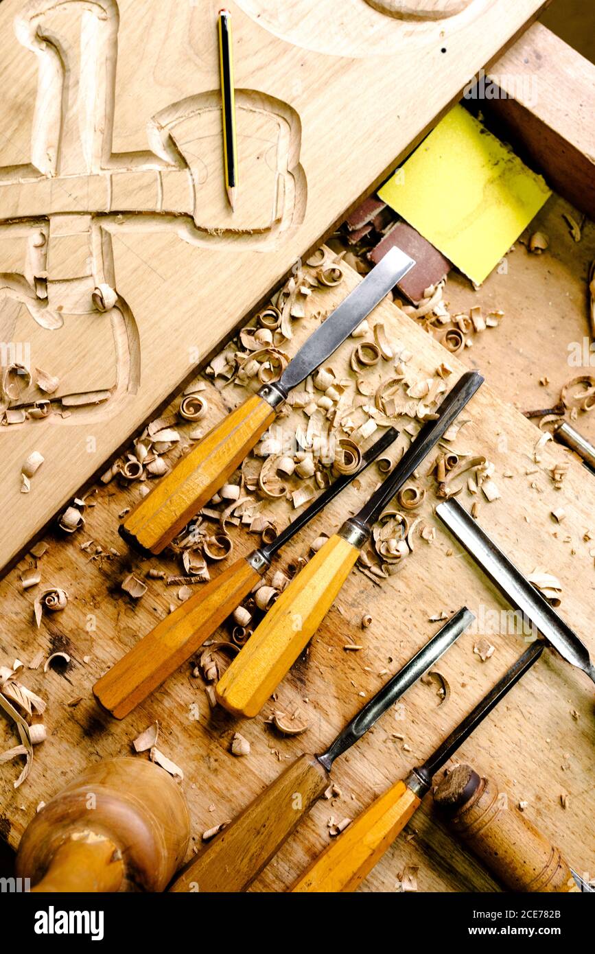 Top view of set of various chisels for wood carving placed on messy workbench with wood shavings Stock Photo