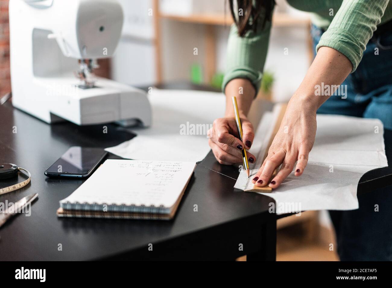 unrecognizable seamstress standing leaned forward while using straightedge at table with papers and scissors in loft style studio Stock Photo