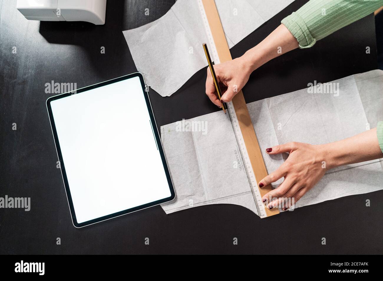 from above crop seamstress standing leaned forward while using straightedge at table with papers in studio Stock Photo