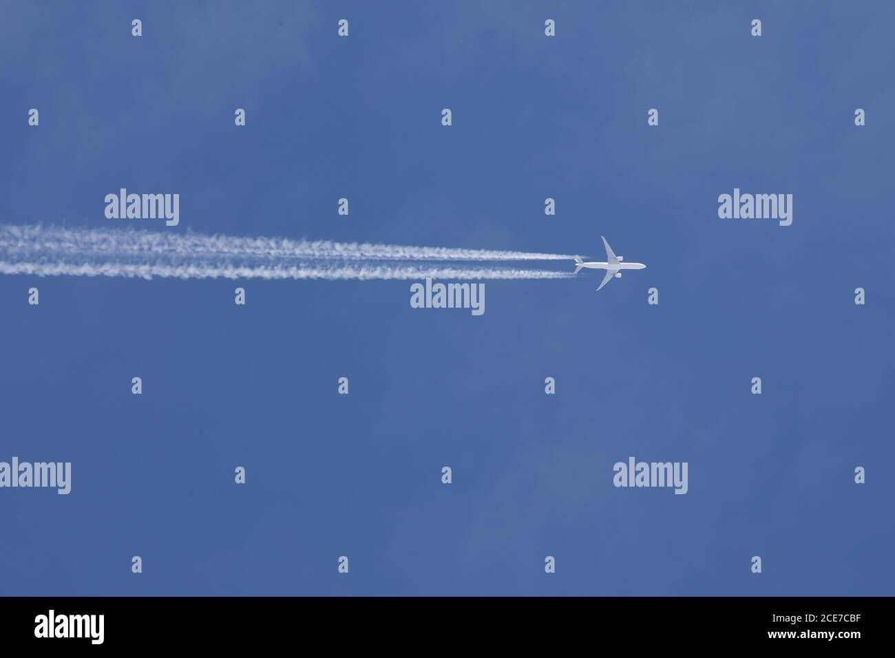 One passenger plane high in the sky with chemtrails with a blue sky Stock Photo