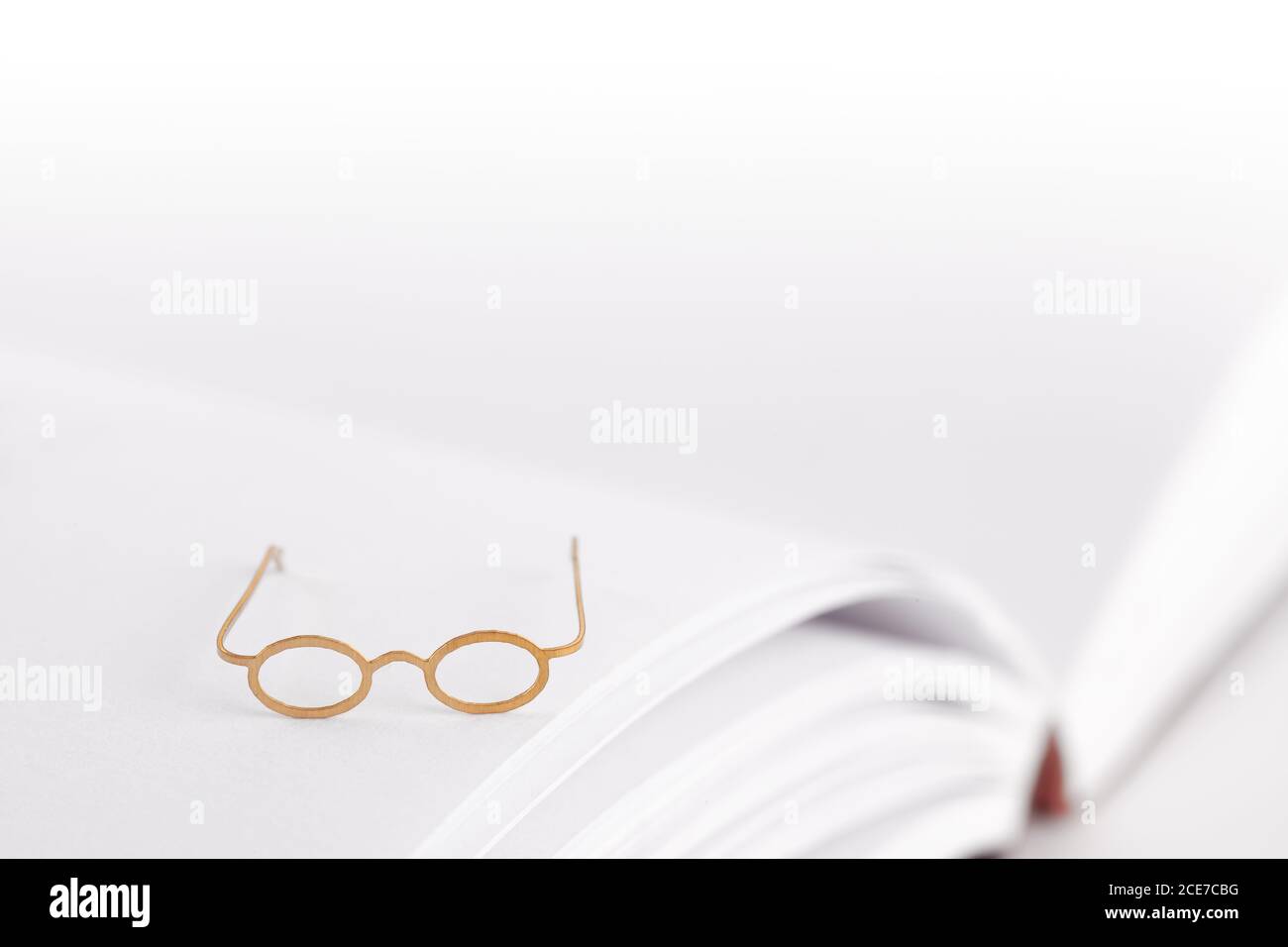 Tiny reading glasses on an open book with blank pages. White background with text space. No words Stock Photo