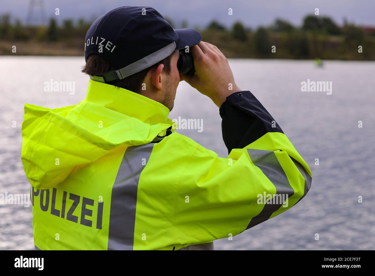 Dresden, Germany. 28th Aug, 2020. A police officer in a yellow-green  raincoat with the inscription Police on his back is looking at a body of  water with binoculars. Credit: Tino Plunert/dpa-Zentralbild/ZB/dpa/Alamy  Live