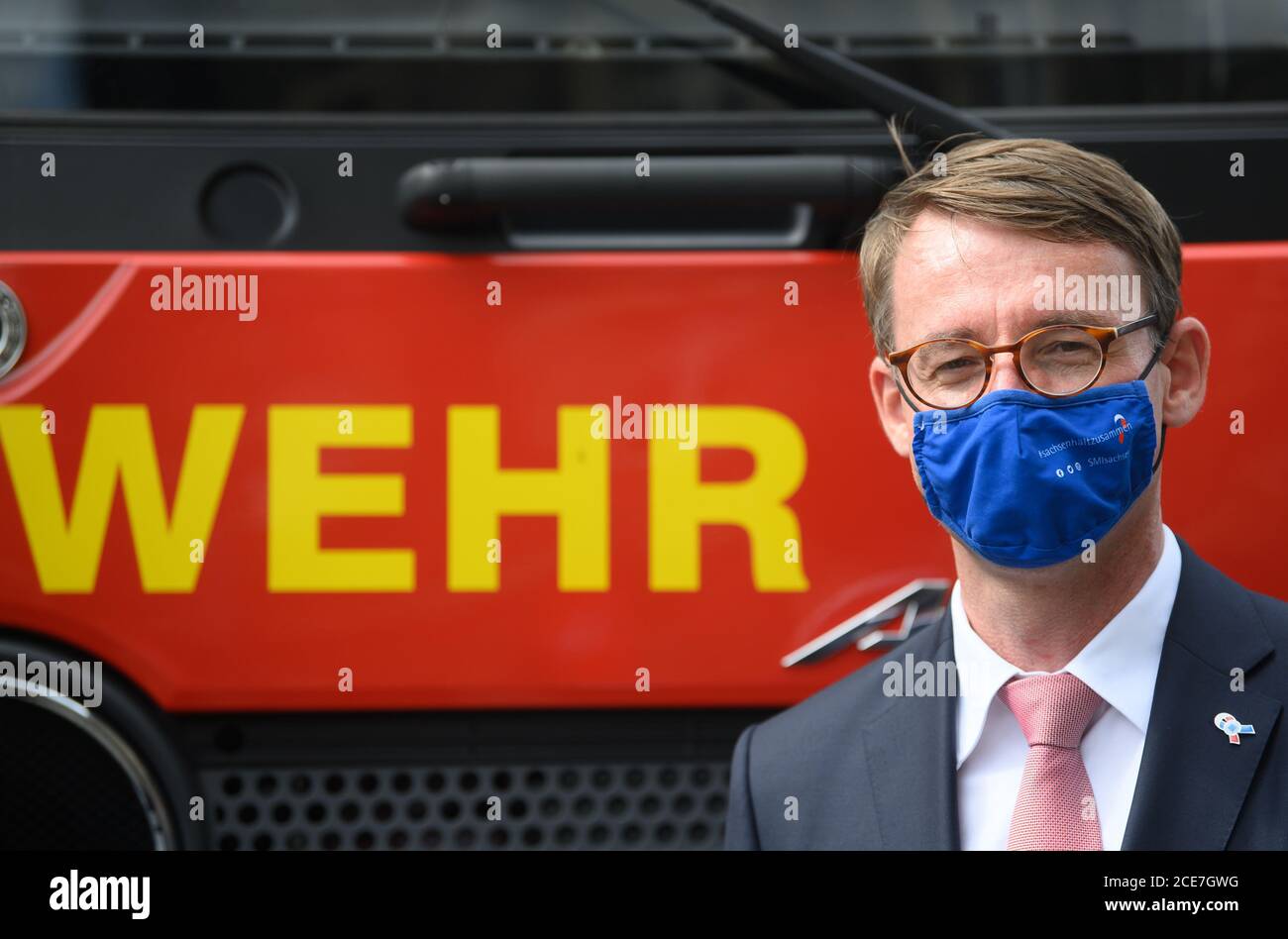 28 August 2020, Saxony, Dresden: Roland Wöller (CDU), Minister of the Interior of Saxony, stands in front of a fire engine during the handover of 23 new emergency vehicles to the Civil Defence and Disaster Control Service of Saxony, wearing a mouth and nose protection. Together with the President of the Federal Office for Civil Protection and Disaster Assistance, the Minister handed over 19 crew transport vehicles and four fire-fighting vehicles. The fleet has a total value of more than 1.8 million euros and is financed partly by the Federal Government and partly by the Free State of Saxony. P Stock Photo