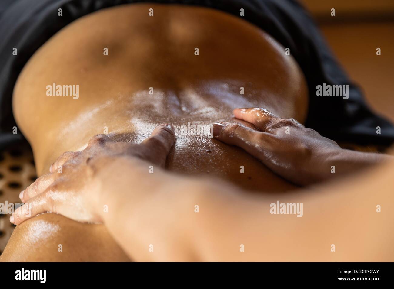 Crop anonymous master performing ayurvedic massage with aromatic oil on back of relaxed customer in modern salon Stock Photo