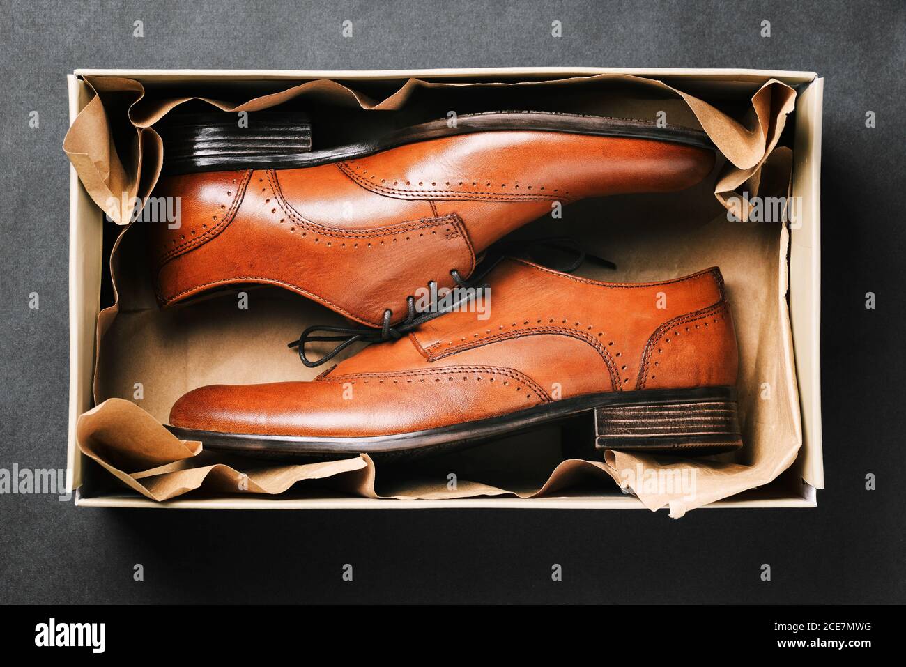 Brown shoes in a box on a black background. New shoes made of genuine leather in the package. Men's fashion classic shoes. Top view of a flat layout Stock Photo