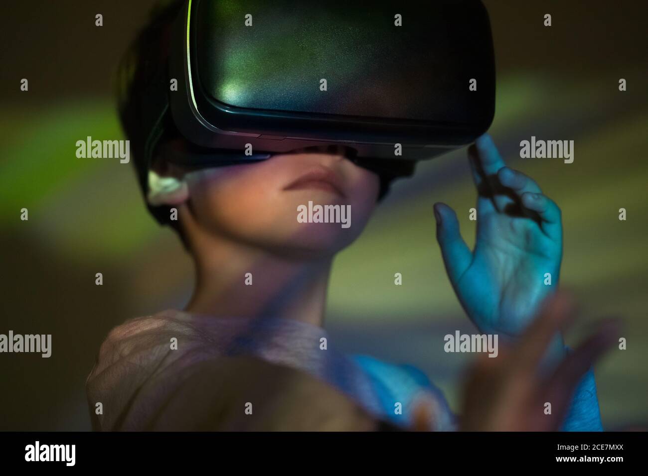 Cute boy wearing VR glasses and exploring virtual reality while standing under colorful projection Stock Photo