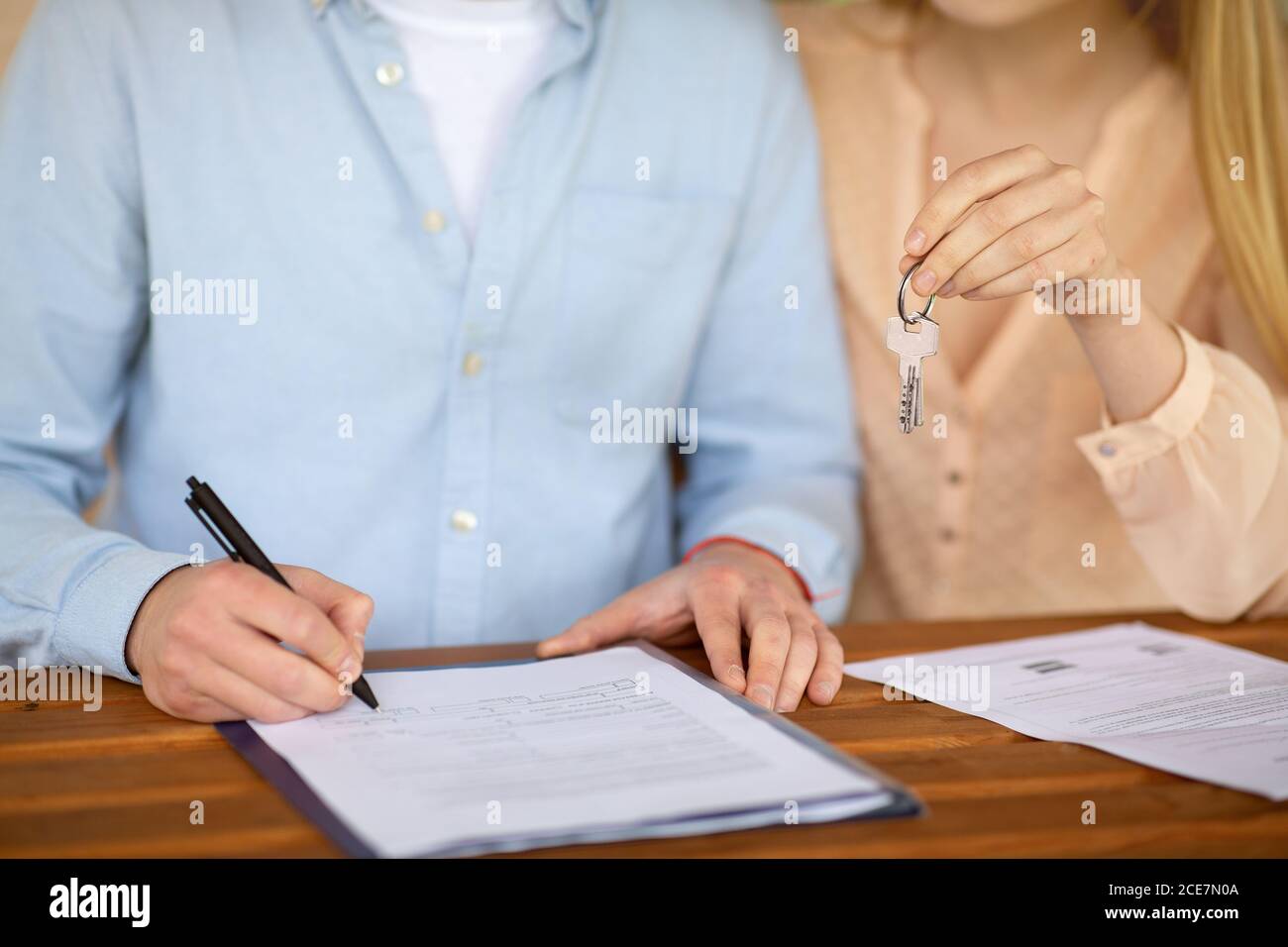 Cropped view of young couple with house key signing real estate purchase agreement at table, close up Stock Photo
