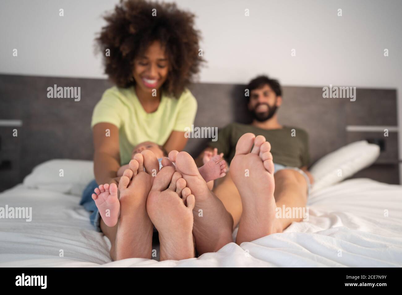 Content multiracial barefoot mother and father lying on bed with cute baby while enjoying weekend together Stock Photo