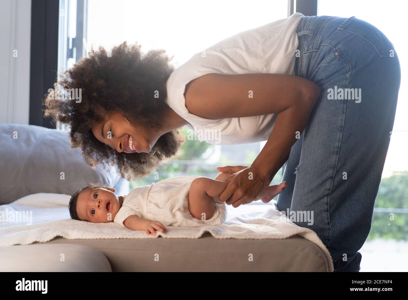 Side view of delighted ethnic African American Woman playing with cute baby on sofa at home Stock Photo