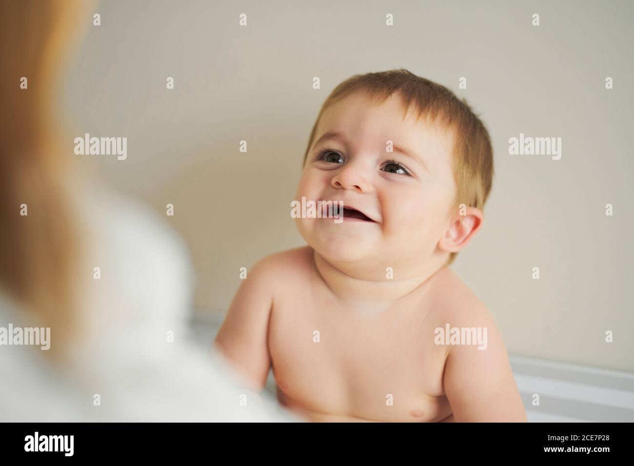 Little cheerful baby looking at anonymous mother and enjoying time together at home Stock Photo