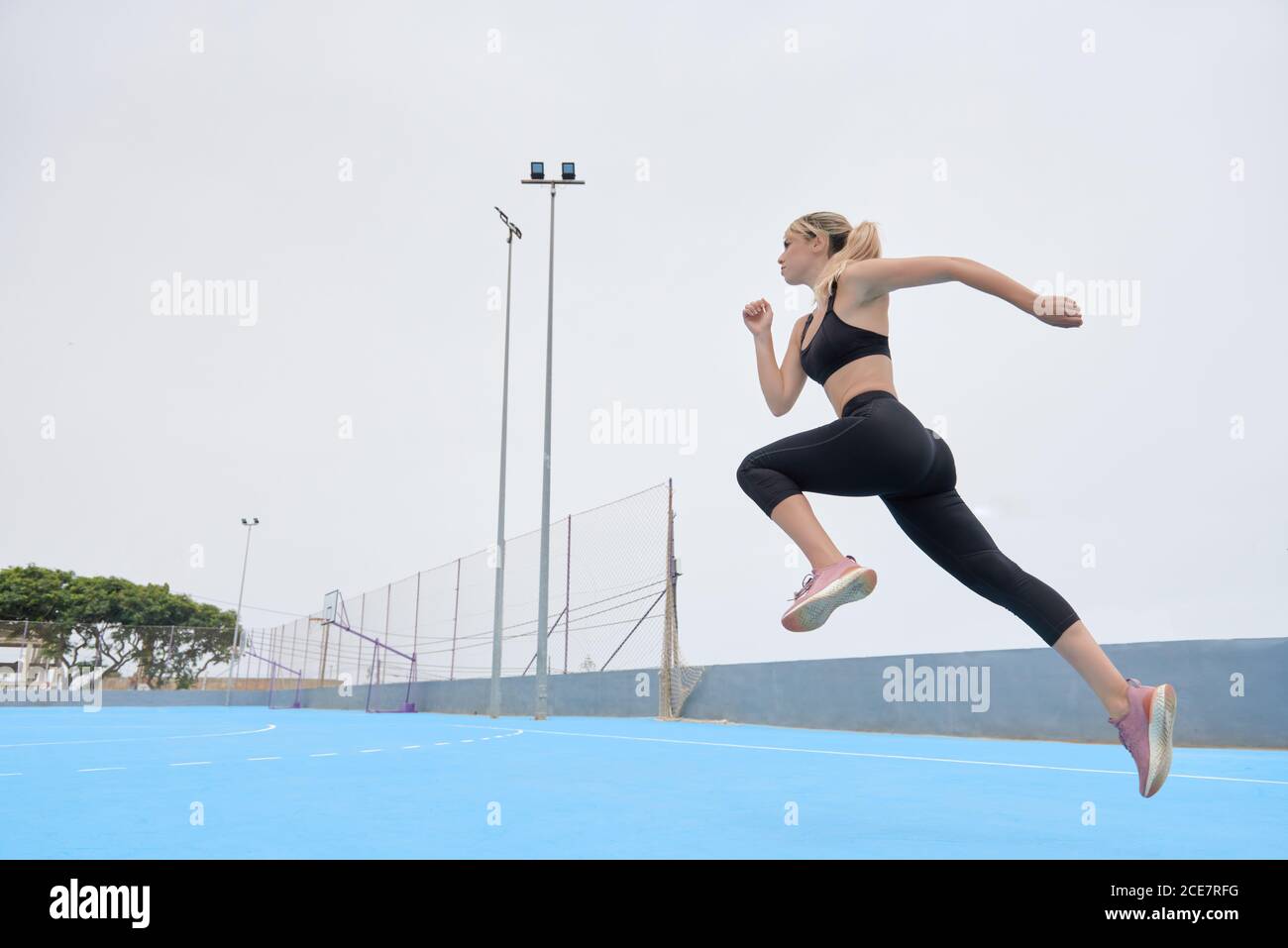Low angle side view of determined confident young female athlete in fitness outfit jumping on sports ground Stock Photo