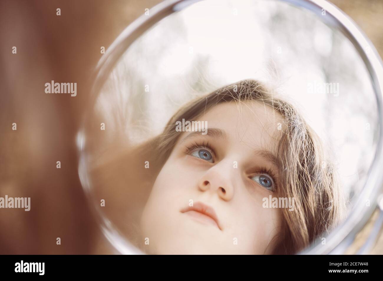Wistful child with blue eyes and brown hair looking away while reflecting in round mirror in apartment in daylight Stock Photo