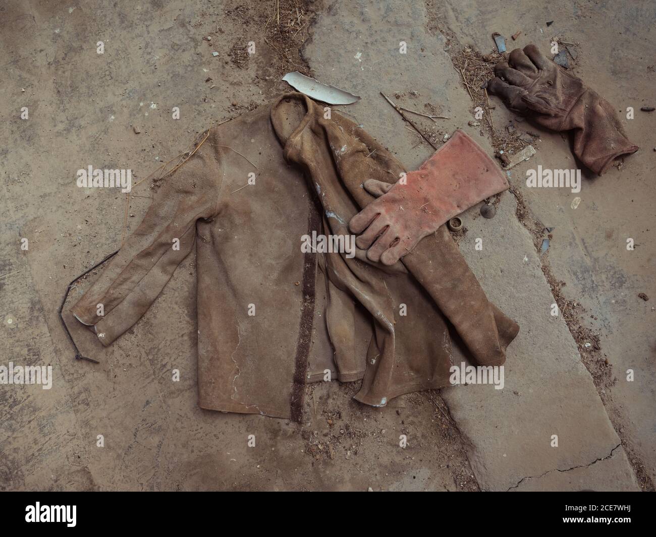 Top view of part of dirty mans uniform representing used brown jacket and heat resistant gloves on shabby sidewalk in street Stock Photo
