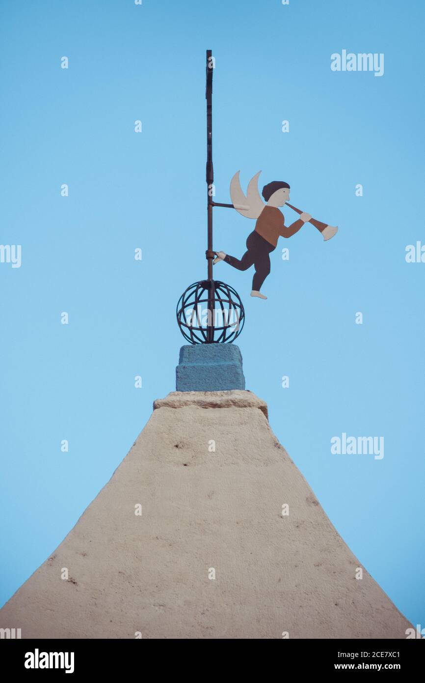 From below of weather vane in shape of little angle playing musical instrument on cross of temple dome under blue sky Stock Photo