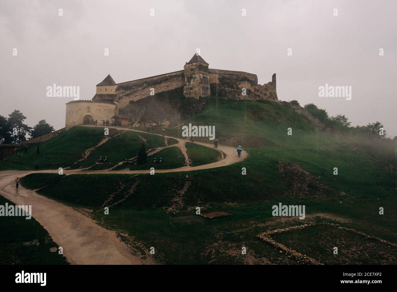 Amazing landscape of medieval Rasnov Fortress in Romania located on green hill with narrow curvy footpath under heavy cloudy sky Stock Photo