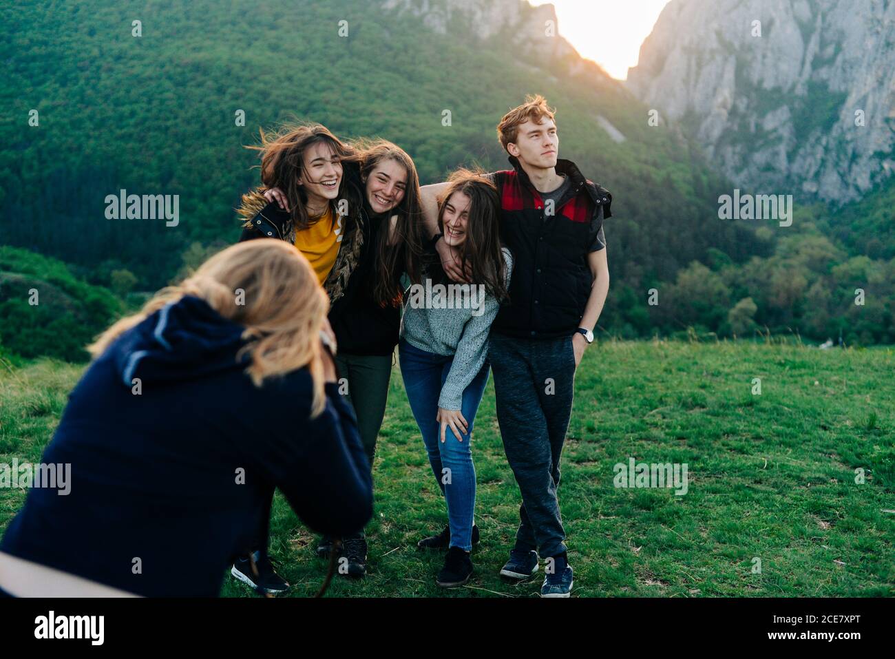 Back view of anonymous female taking picture of company of cheerful friends standing on green lawn in highlands during vacation in Transylvania Stock Photo