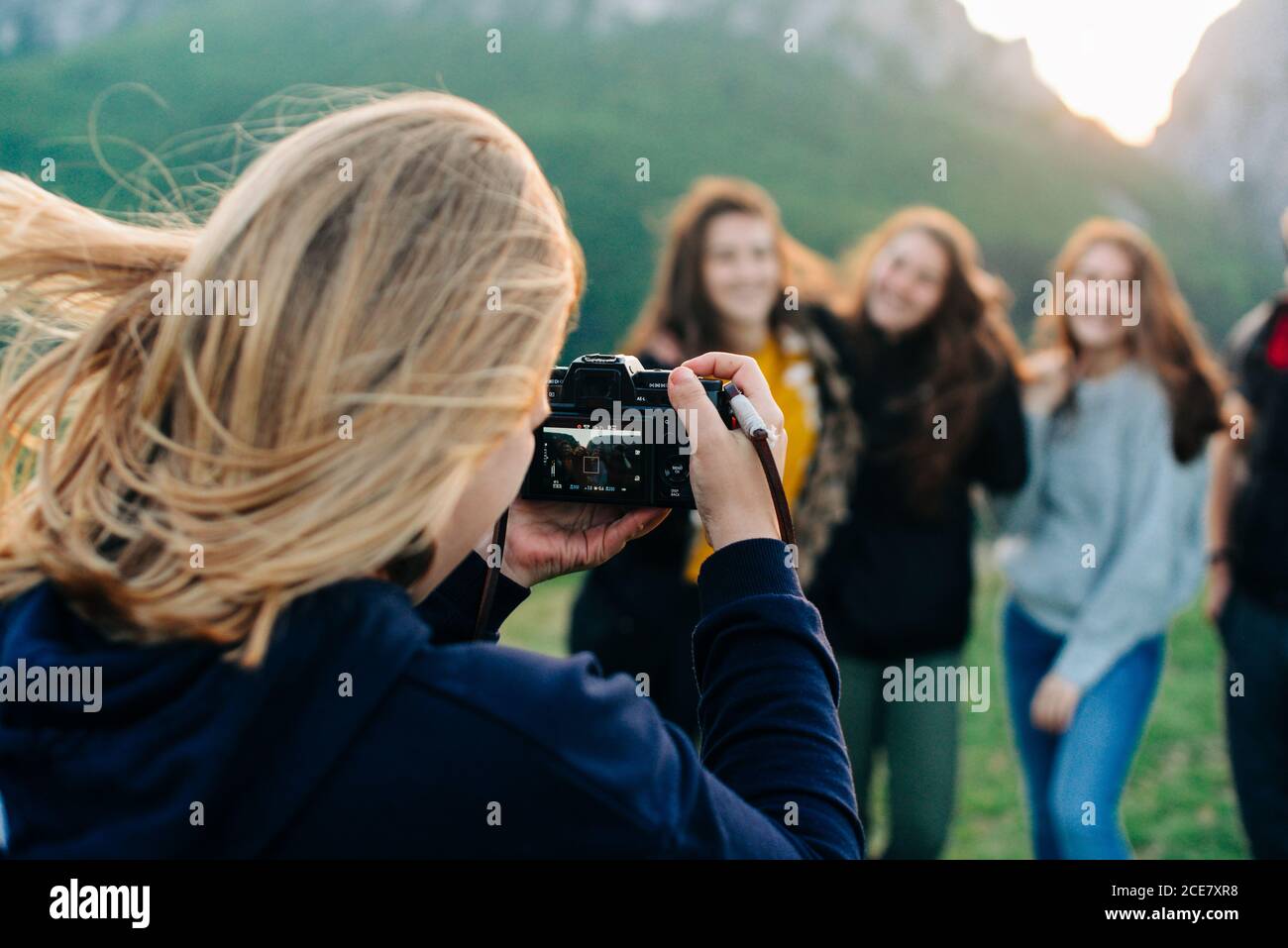 Back view of anonymous female taking picture of company of cheerful friends standing on green lawn in highlands during vacation in Transylvania Stock Photo