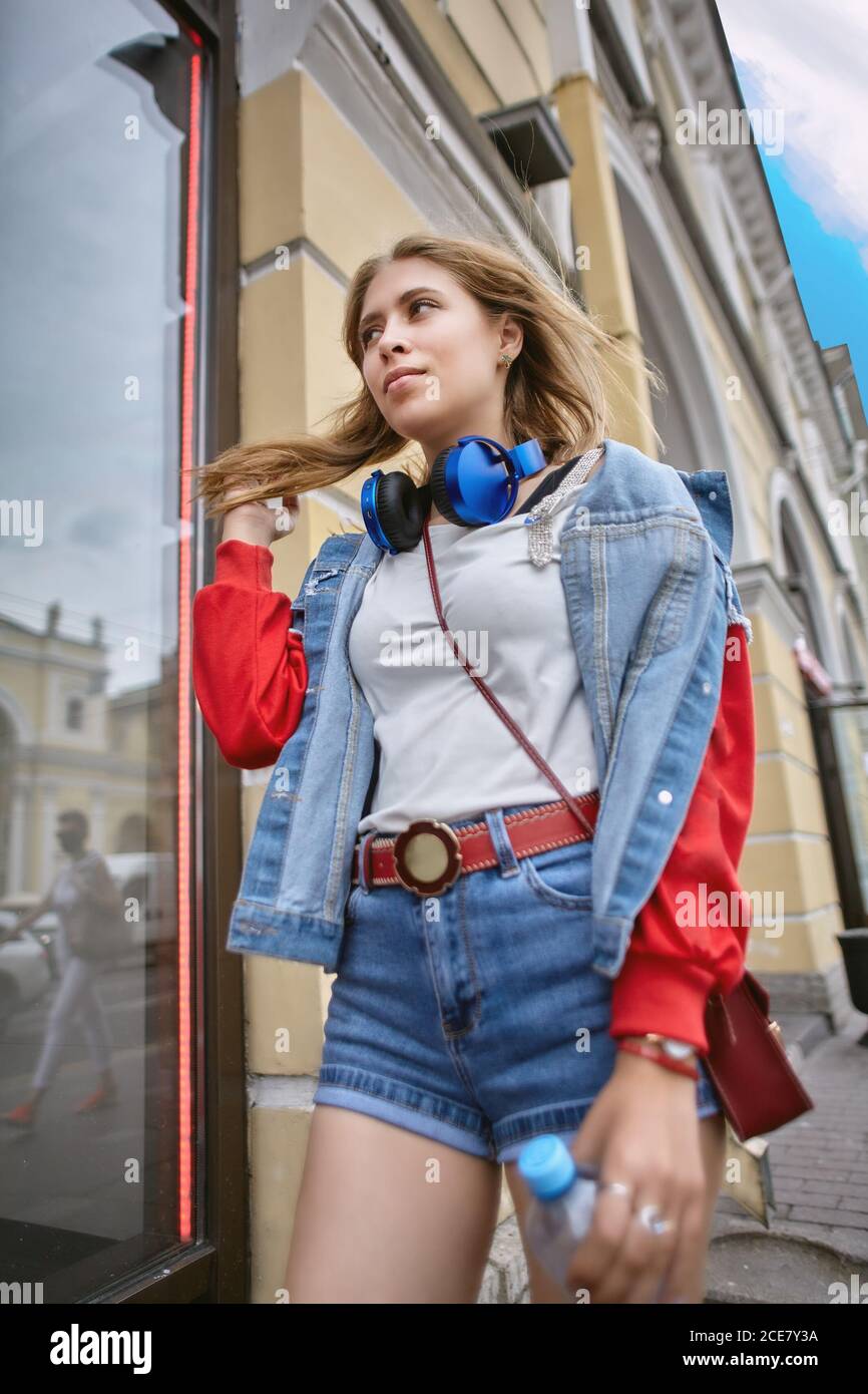 Woman dressed in street style walks down the avenue of a European city. A young white female in denim shorts steps through the center of the metropoli Stock Photo