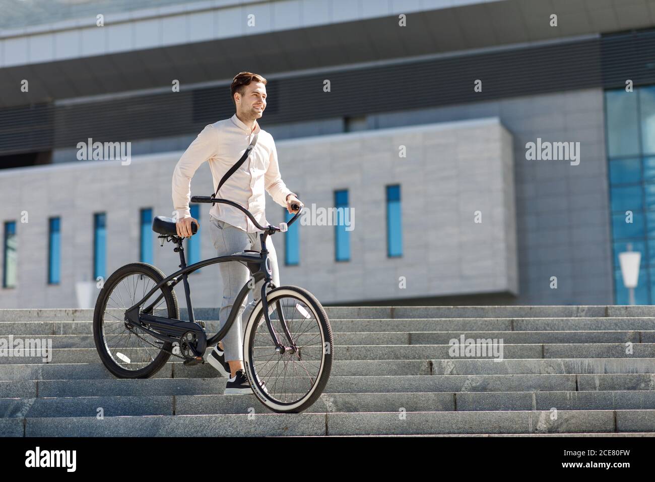 Businessman holds bicycle in his hands and looking away, goes on stairs Stock Photo