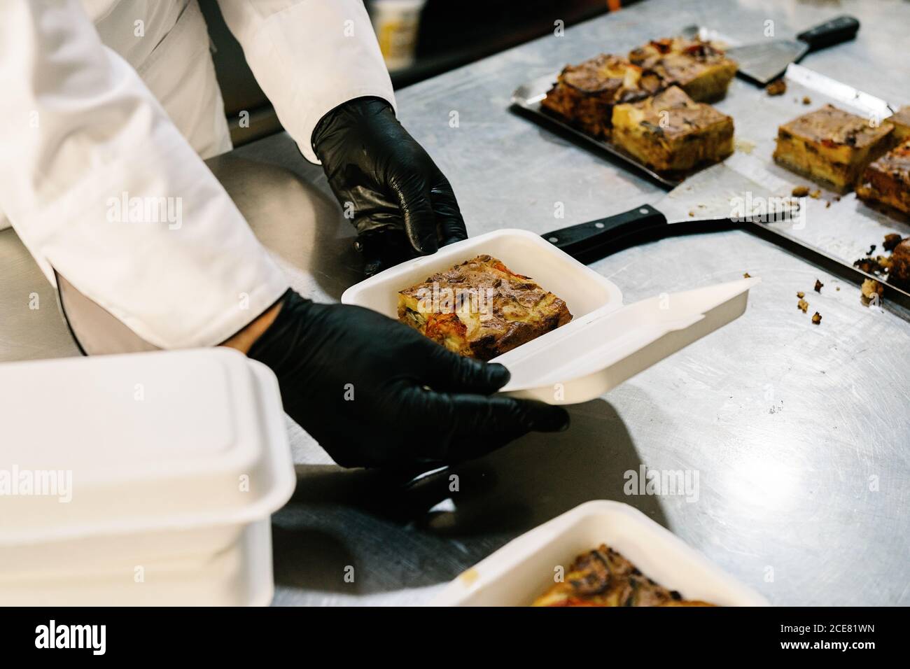 Crop faceless cook wearing latex gloves and uniform packing yummy baked