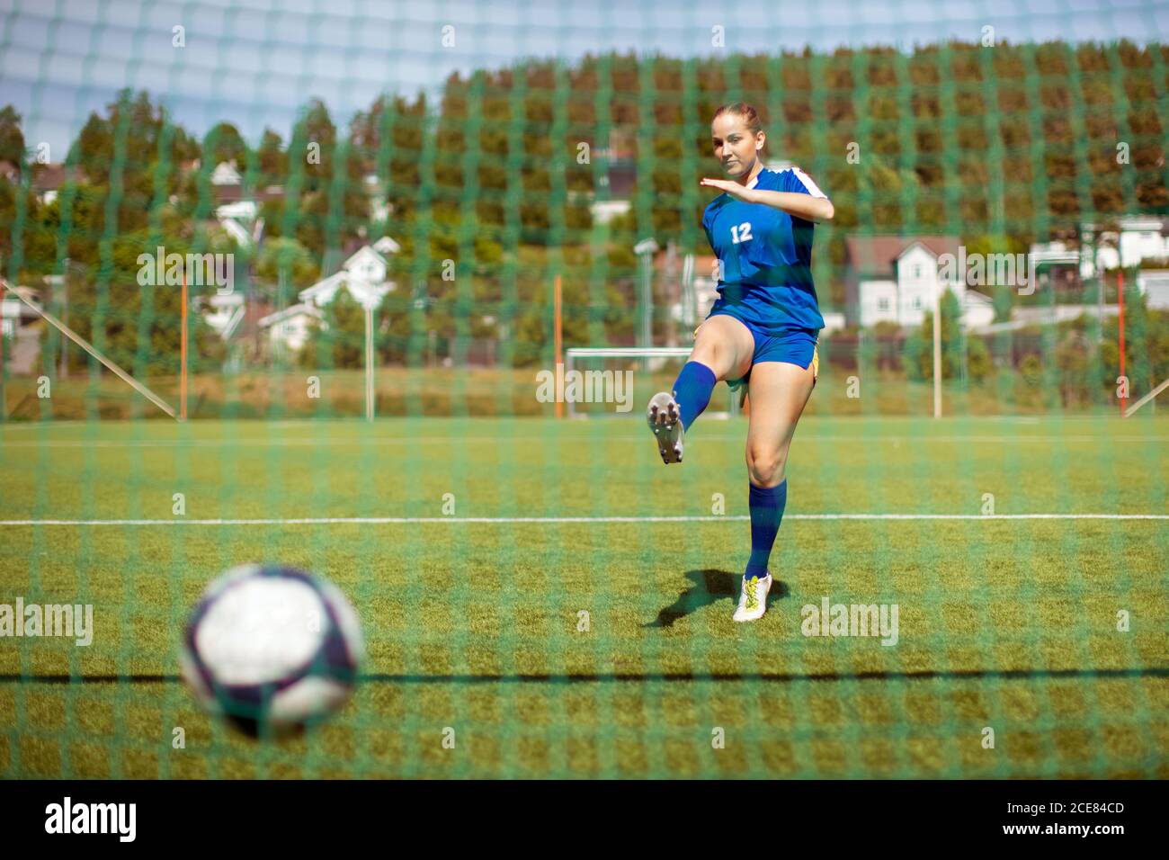 Female athlete shooting ball into goal while playing football on field Stock Photo