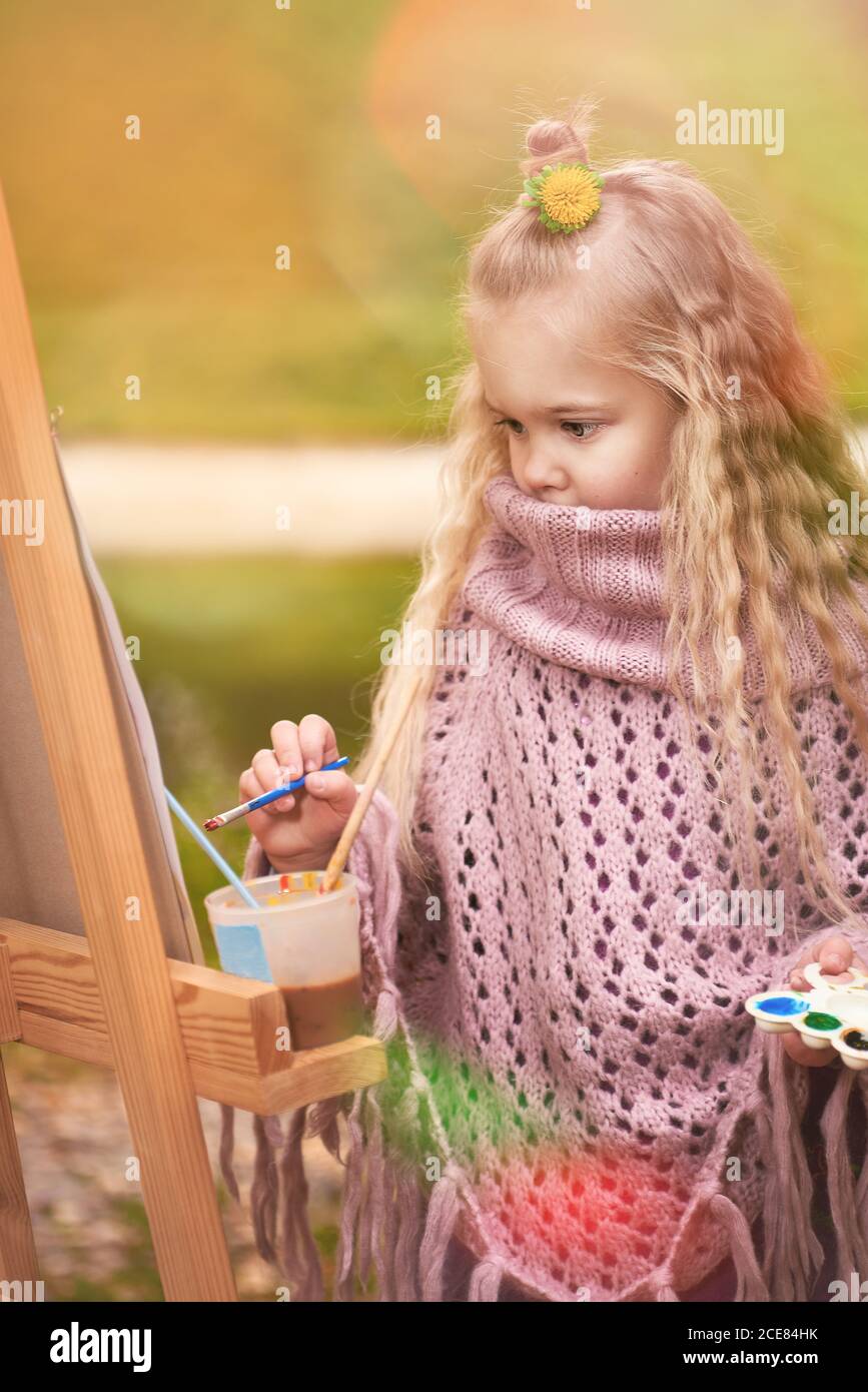 little girl artist paints a picture on an easel in autumn in the park ...