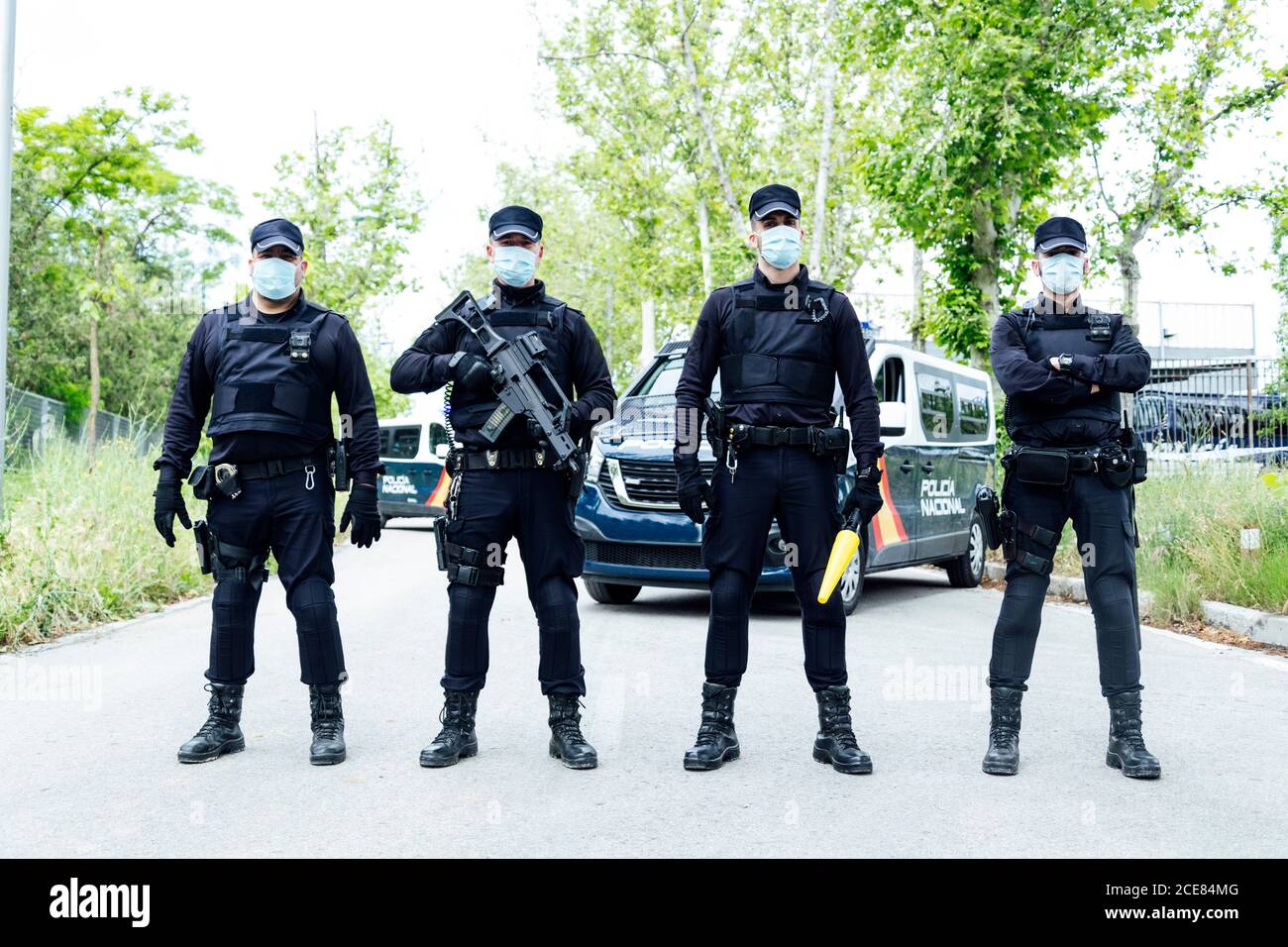 Full body squad of Spanish police officers in protective gears with guns wearing medical masks during patrolling street Stock Photo