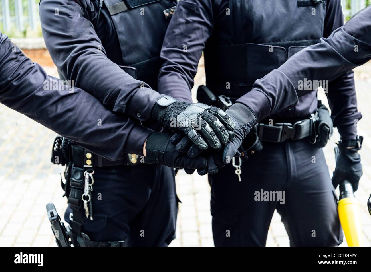 anonymous police officers in protective gears and medical masks armed with guns and batons putting hands together while preparing for operation Stock Photo