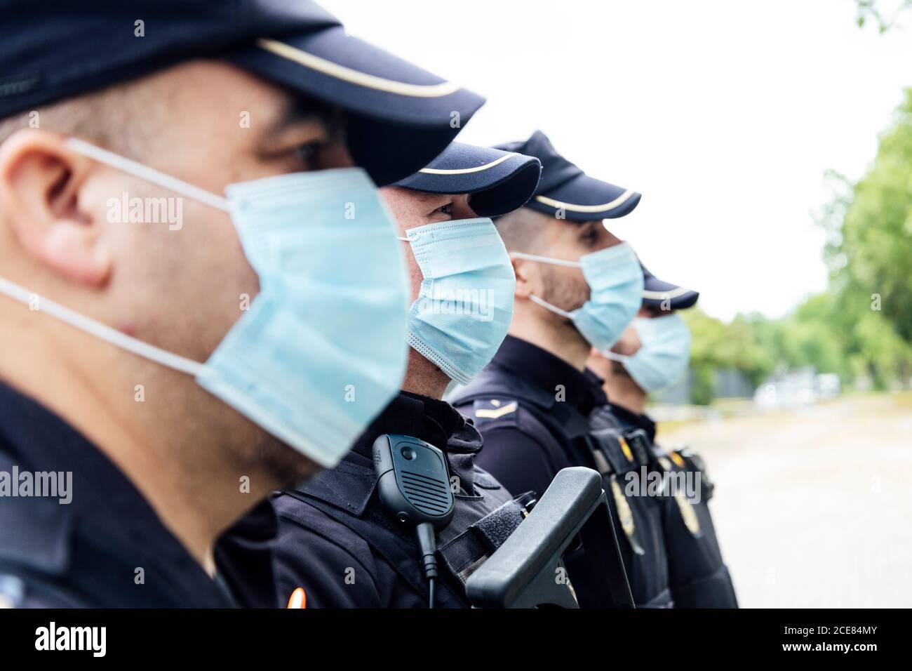 Full body squad of Spanish police officers in protective gears with guns wearing medical masks during patrolling street Stock Photo