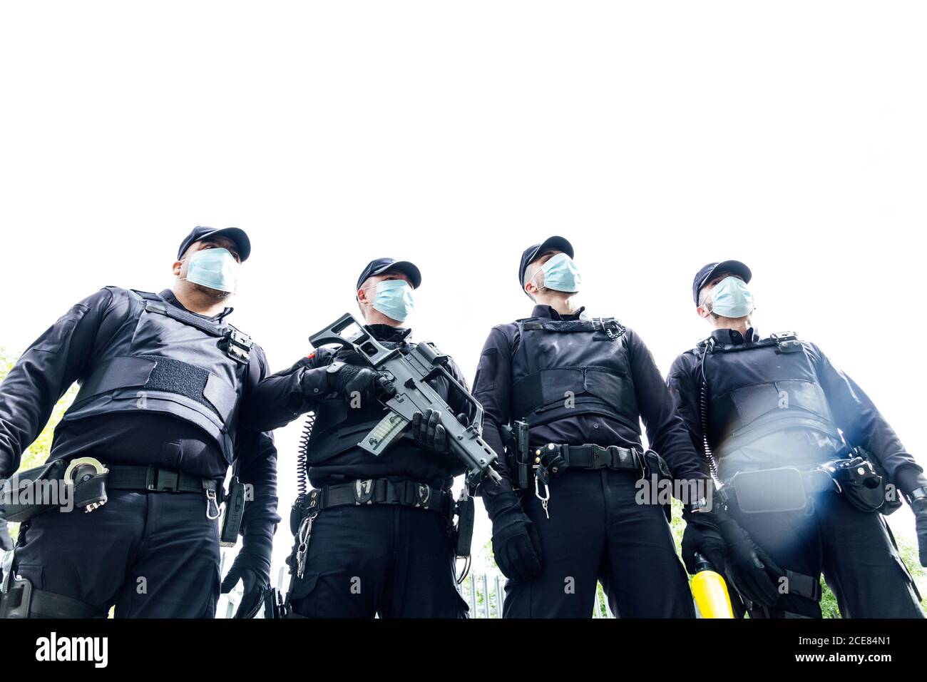 Full body squad of Spanish police officers in protective gears with guns wearing medical masks during patrolling street Stock Photo