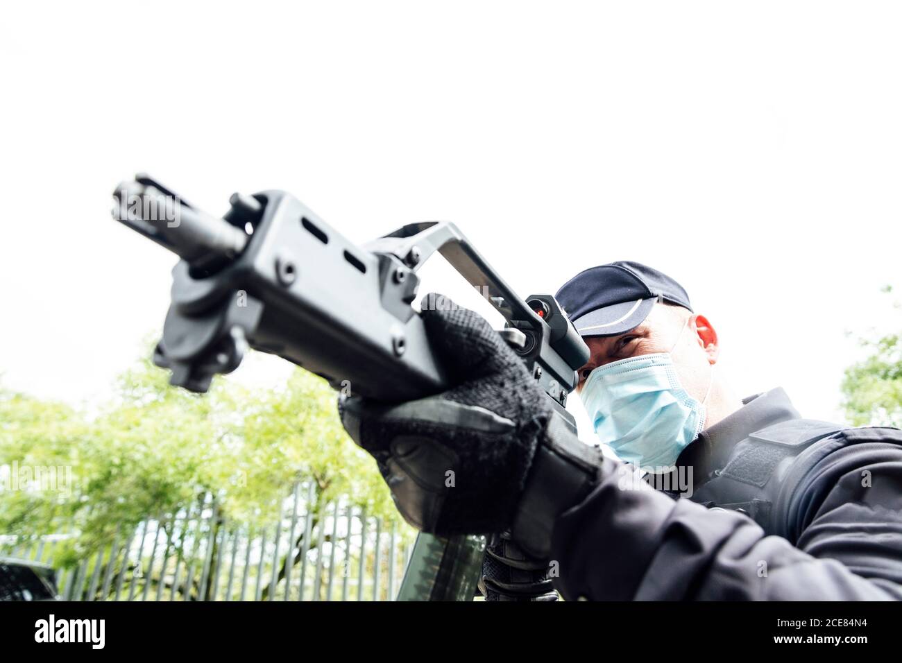 From below of serious spec ops police officer in  protective uniform and medical mask aiming submachine gun during police operation Stock Photo