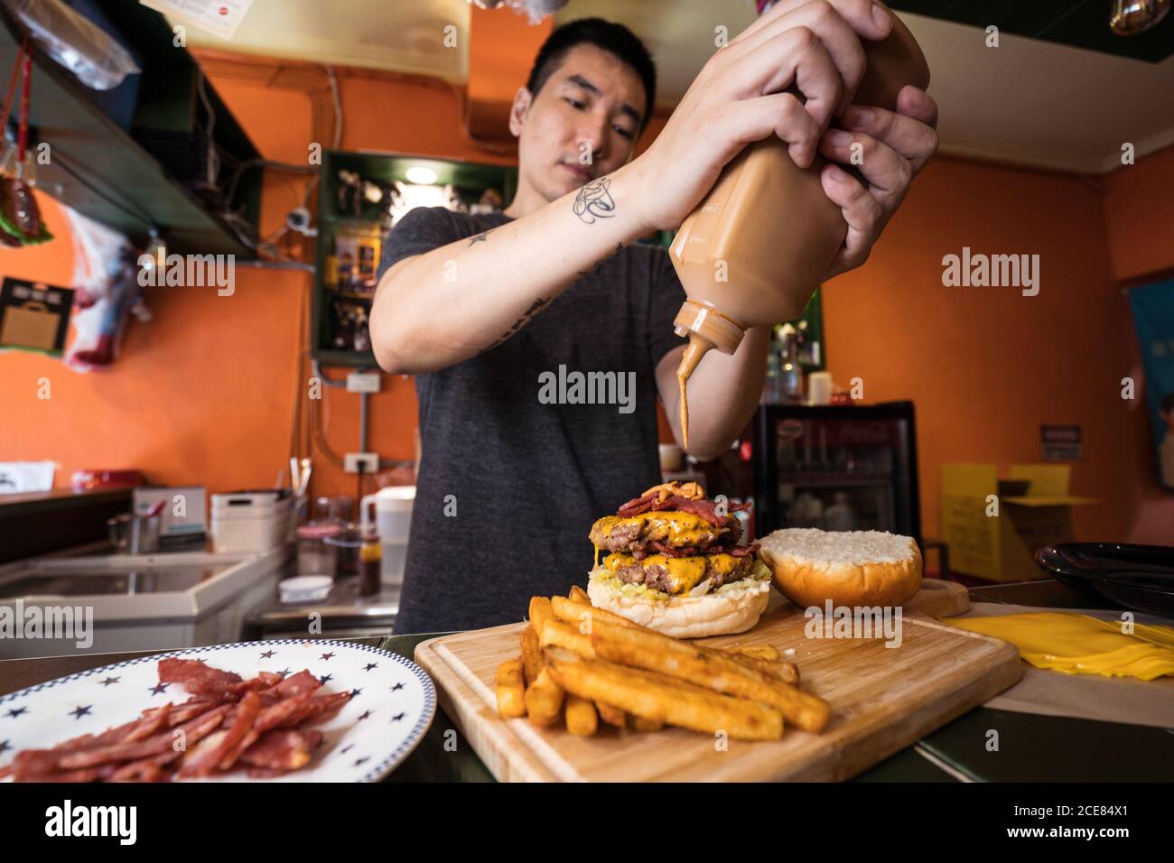 Busy male chef preparing delicious burgers in cafe and pouring sauce on cutlet Stock Photo