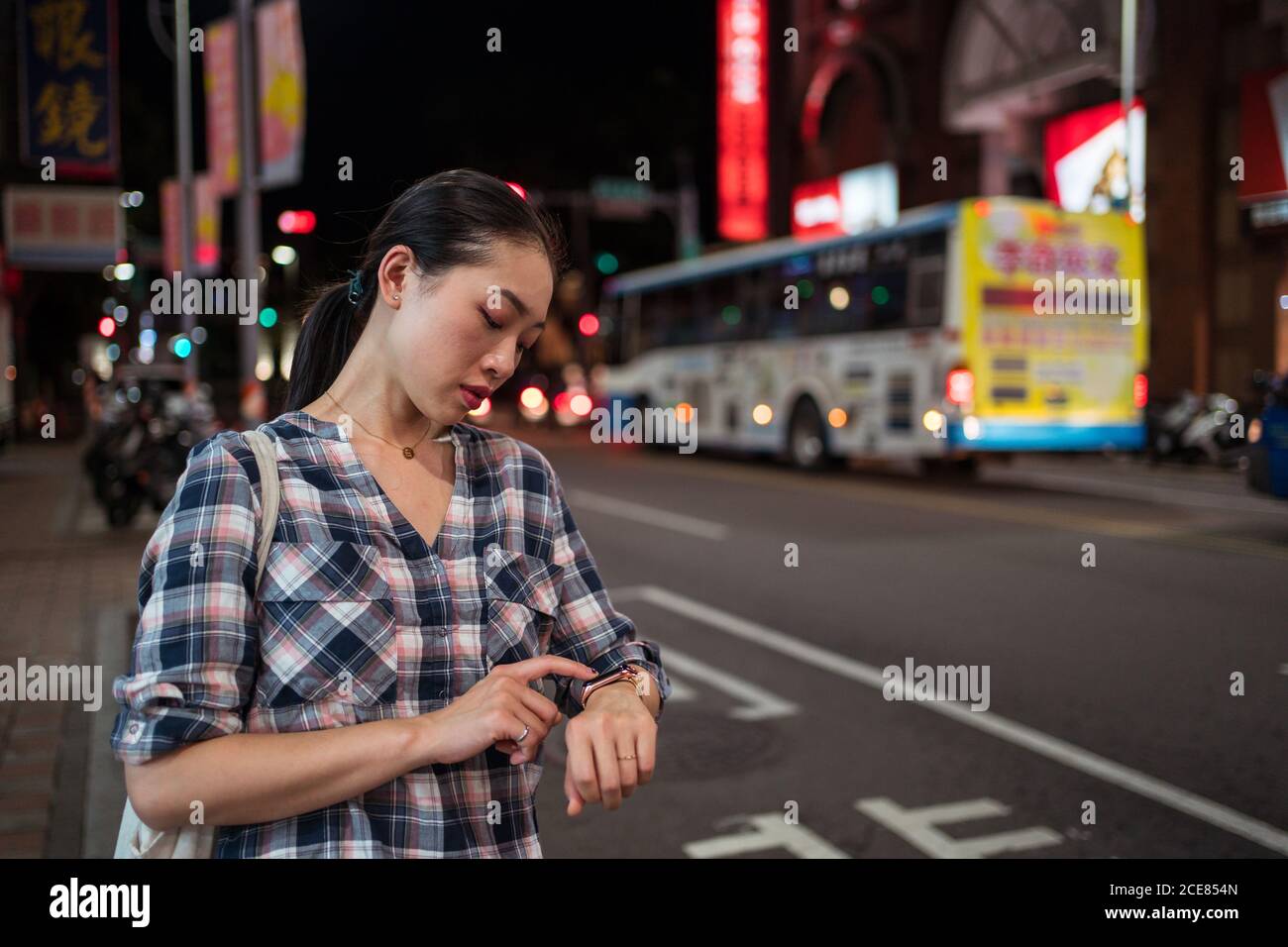 Side view of crop anonymous female in casual checkered shirt checking time on smart bracelet Stock Photo
