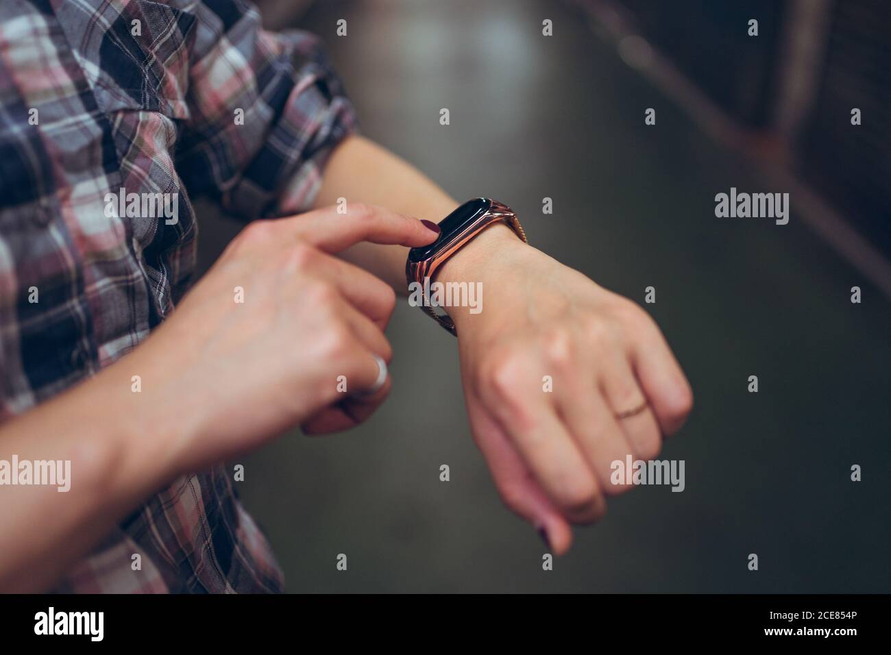 Side view of crop anonymous female in casual checkered shirt checking time on smart bracelet Stock Photo