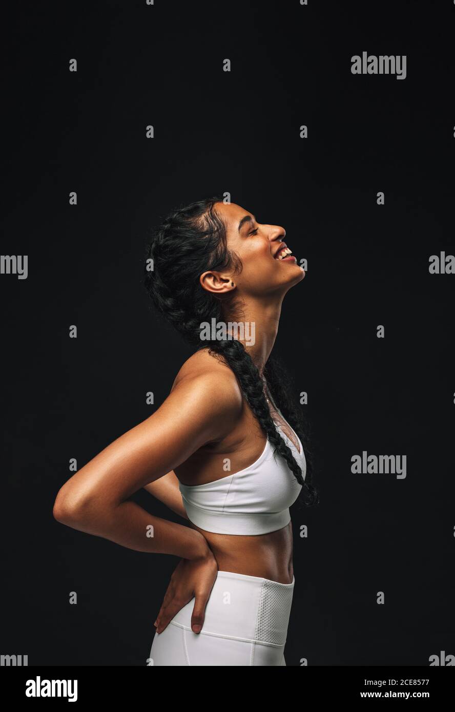 Portrait of a female athlete on black background. Smiling fit woman relaxing after workout. Stock Photo