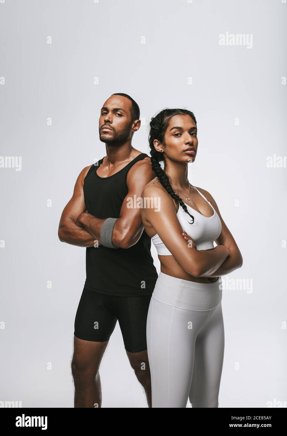 Portrait of male and female athlete standing with arms crossed. Confident fit man and woman standing against white background. Stock Photo