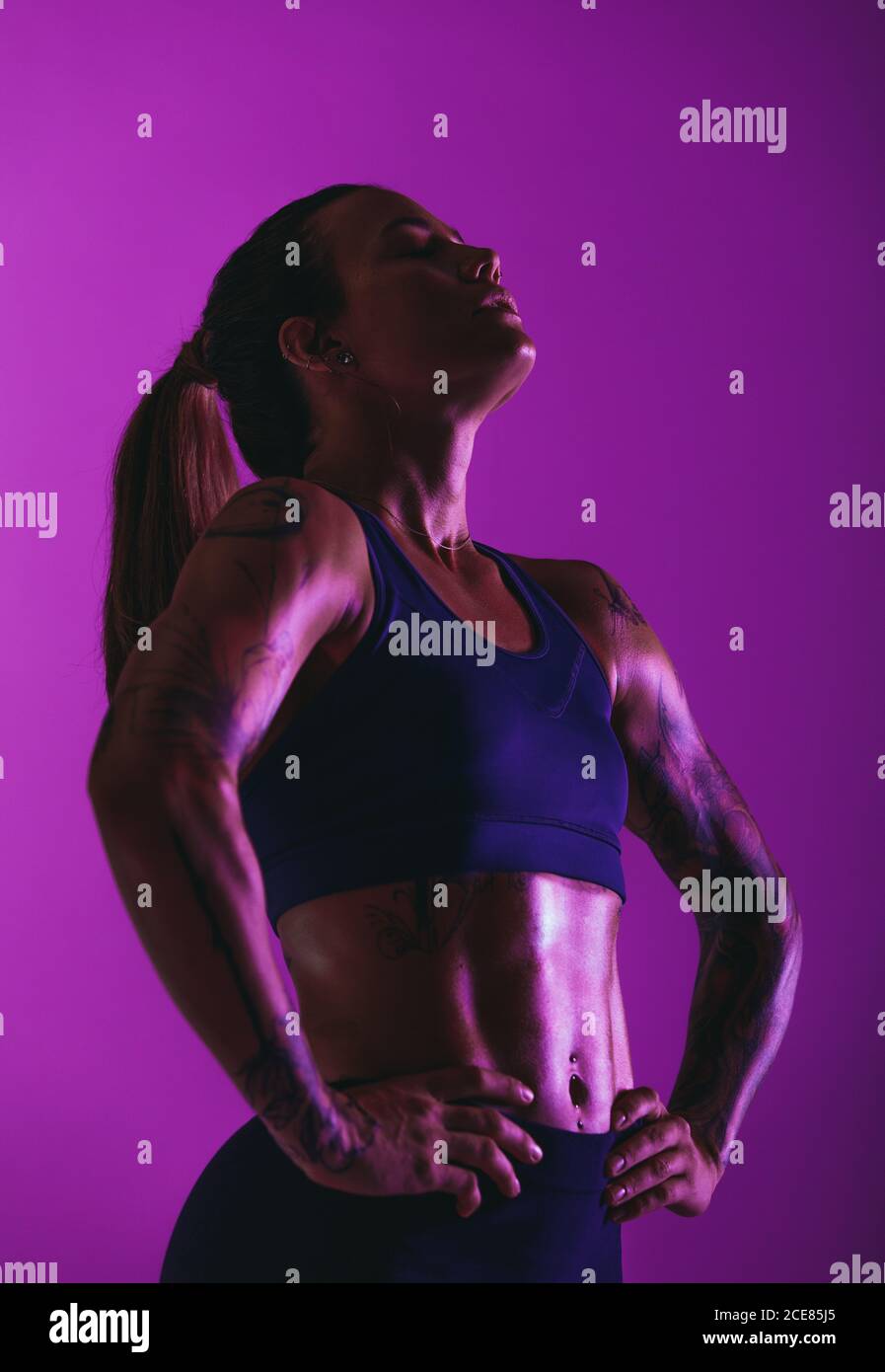 Close up of fit woman doing fitness workout. Portrait of sportswoman on purple background with hands on waist. Stock Photo