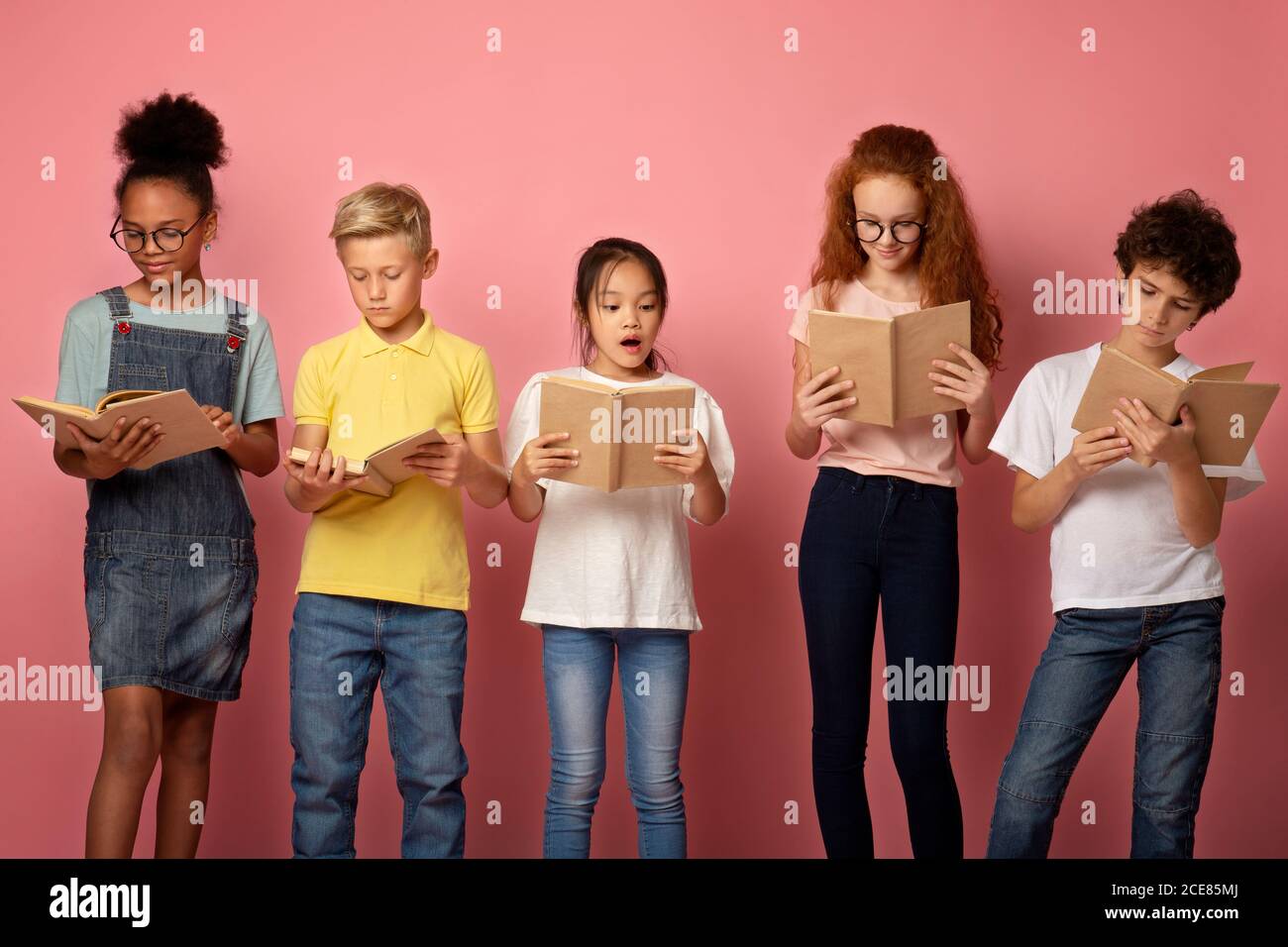 Focused diverse schoolkids reading books over pink background Stock Photo