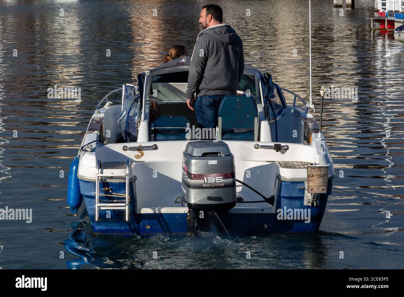 A small speedboat being sailed slowly in a marina Stock Photo