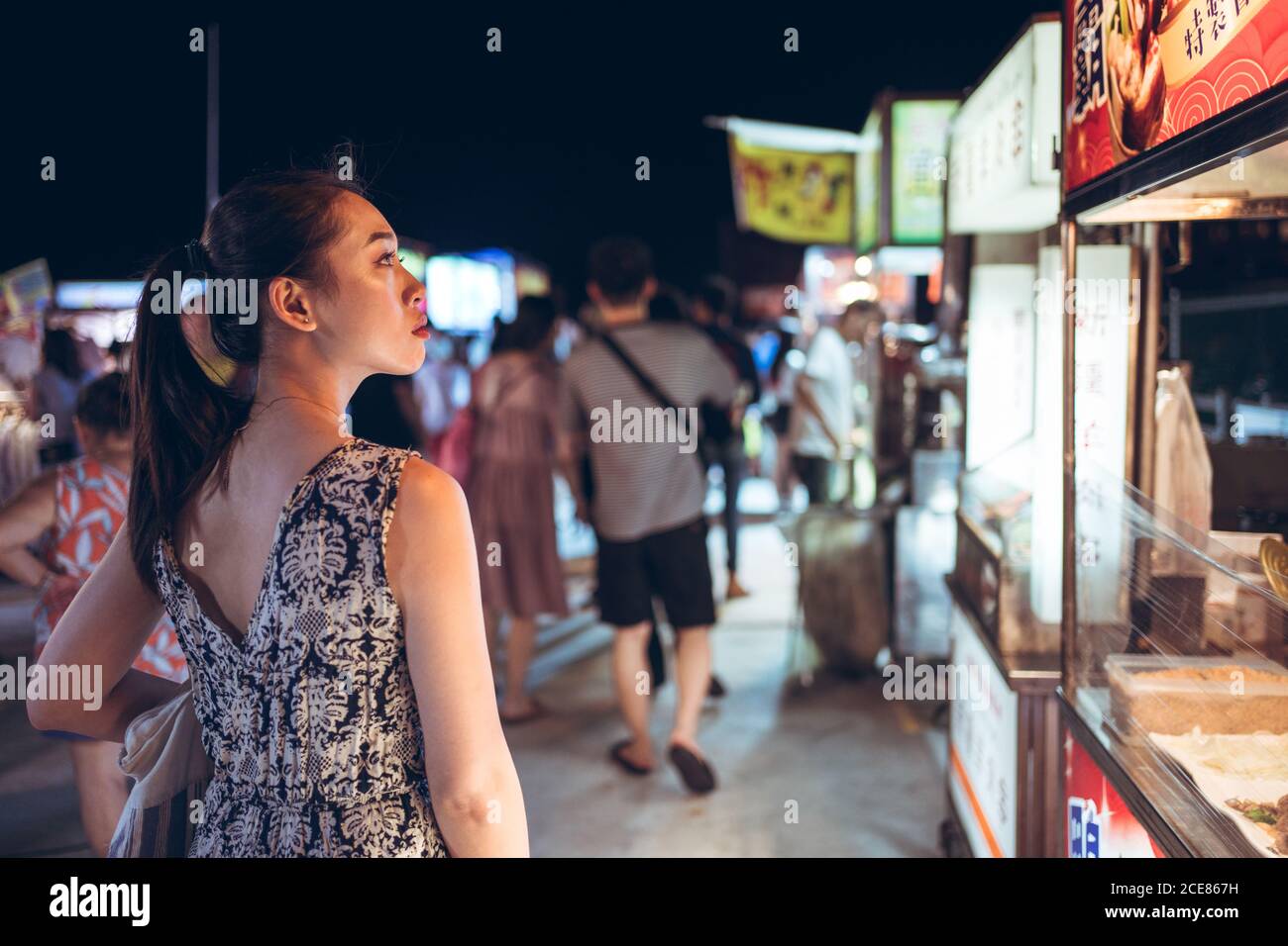 Back view of female in summer dress standing near counter on crowded ...
