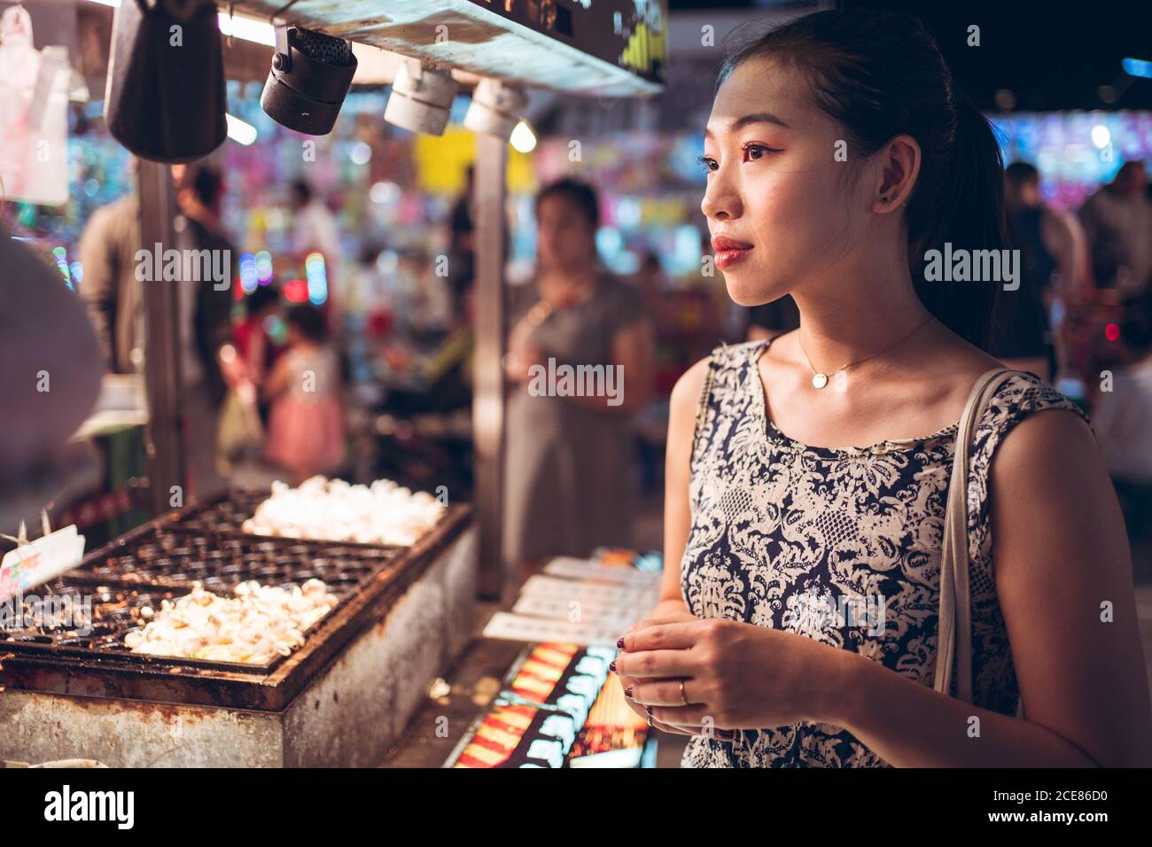 Side view of female in summer dress standing near counter on crowded street in Night Market in Taiwan Stock Photo