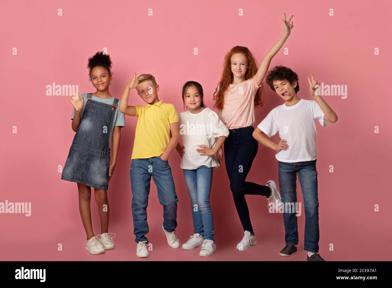 Joyful schoolkids making faces and showing variety of gestures over pink background, full length portrait Stock Photo